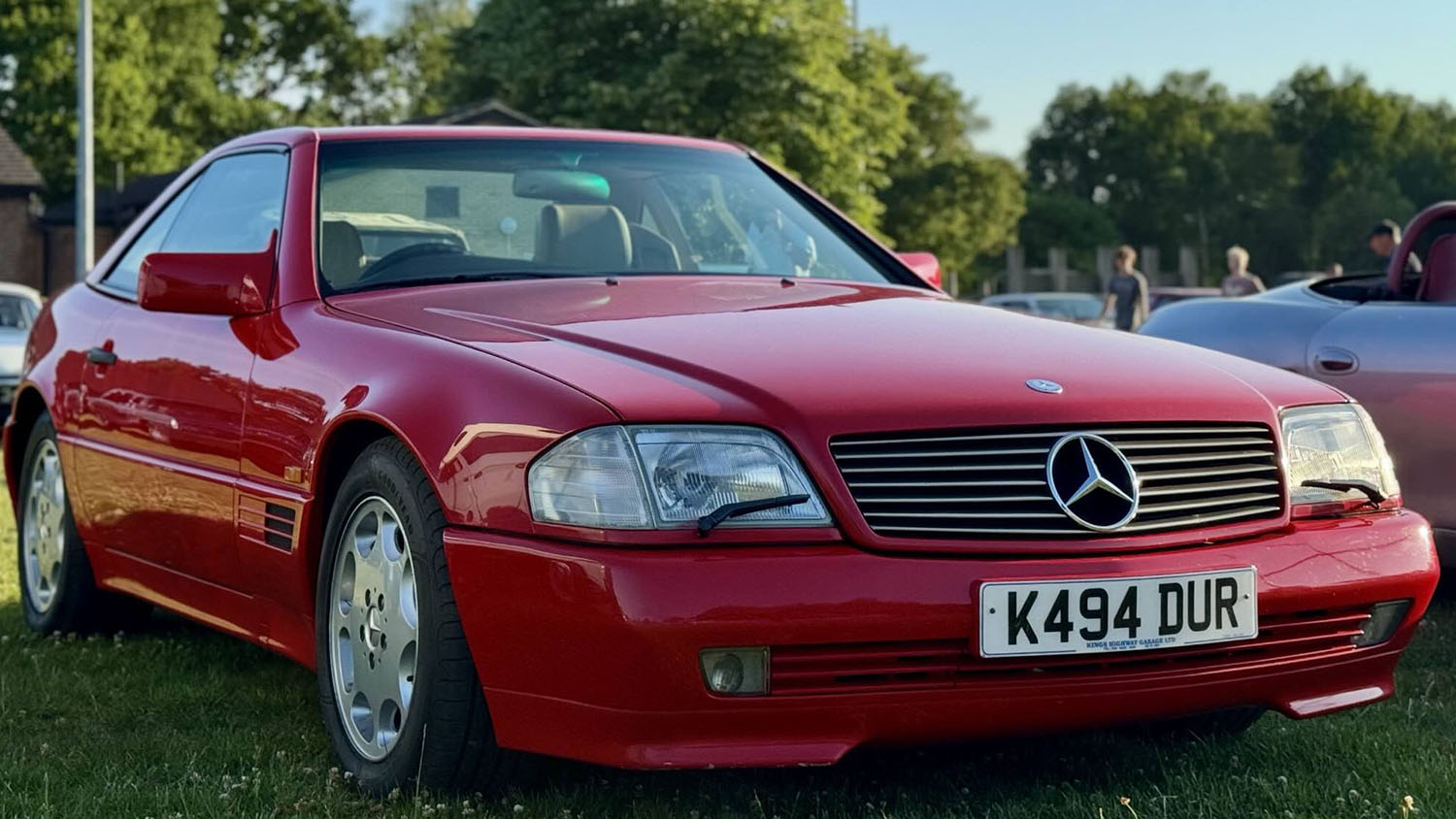 Front view of red Mercedes-Benz SL R129 convertible parked on grass at outdoor event